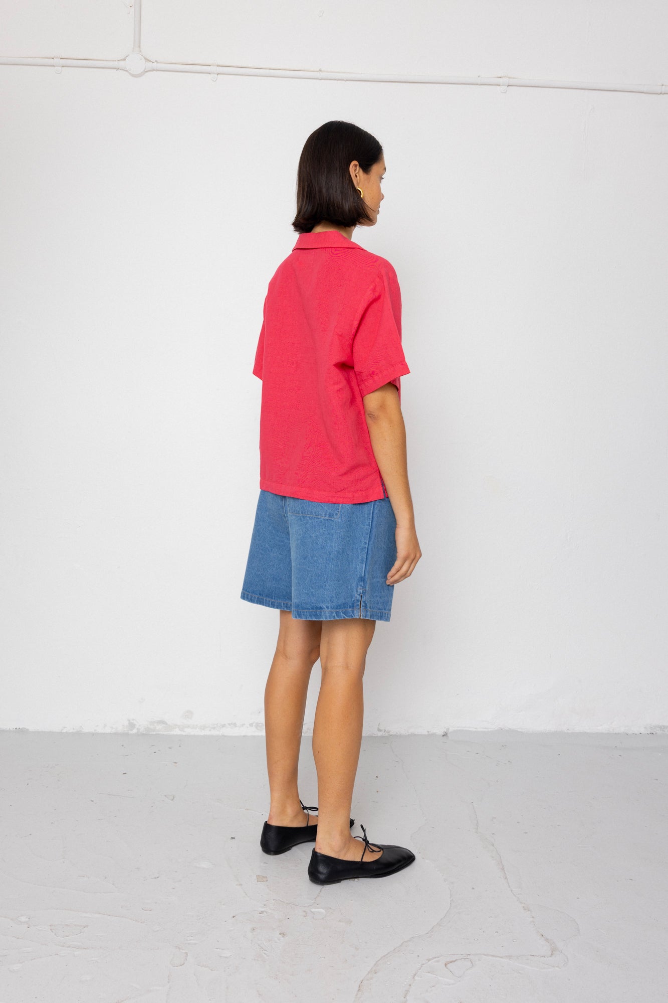 Person wearing a red shirt and blue shorts standing against a white wall.