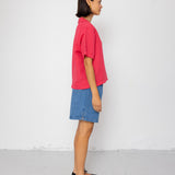 Person wearing a pink shirt and blue denim shorts against a white background