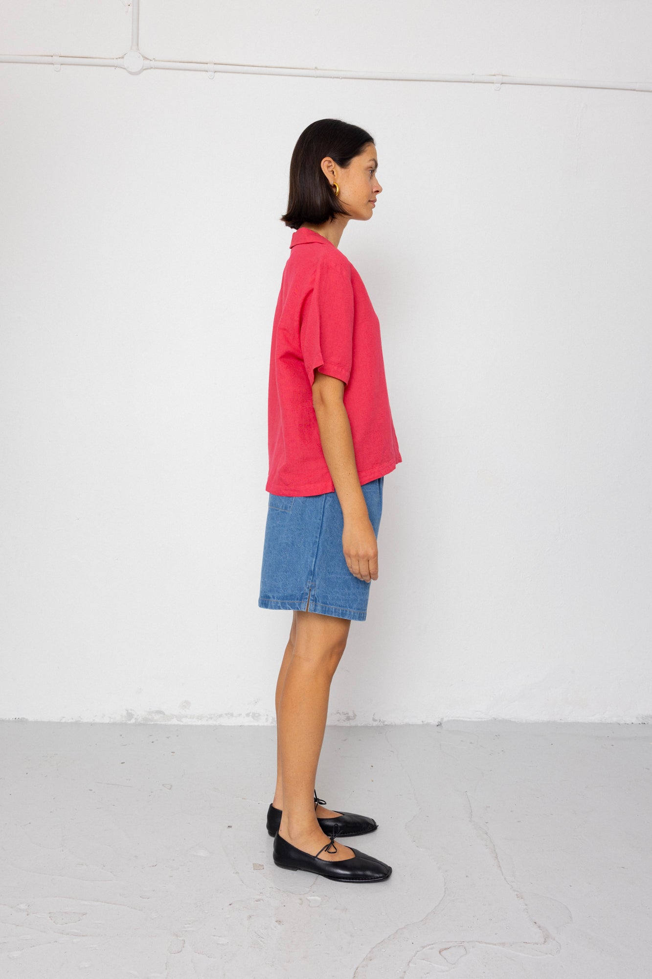 Person wearing a pink shirt and blue denim shorts against a white background