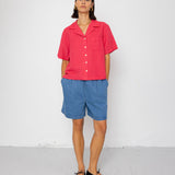 Person wearing a red shirt and blue shorts against a white background