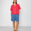 Person wearing a red shirt and blue shorts against a white background