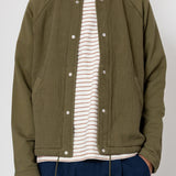 Person wearing a green jacket over a striped shirt with a white background