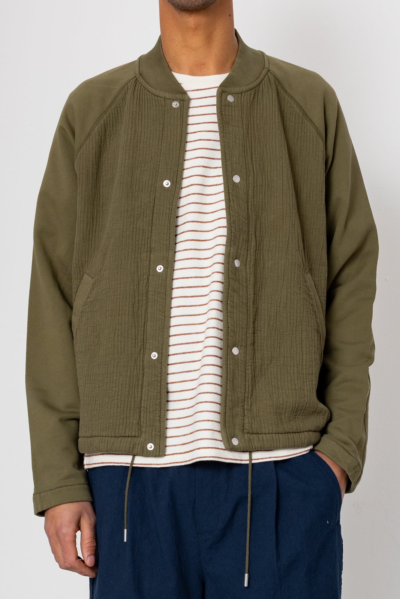 Person wearing a green jacket over a striped shirt with a white background