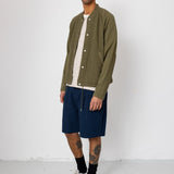 Man wearing a green jacket, striped shirt, navy shorts, and gray sneakers against a white background