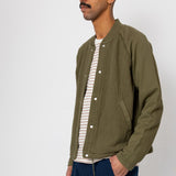 Man wearing a green jacket over a striped shirt with blue pants against a white background