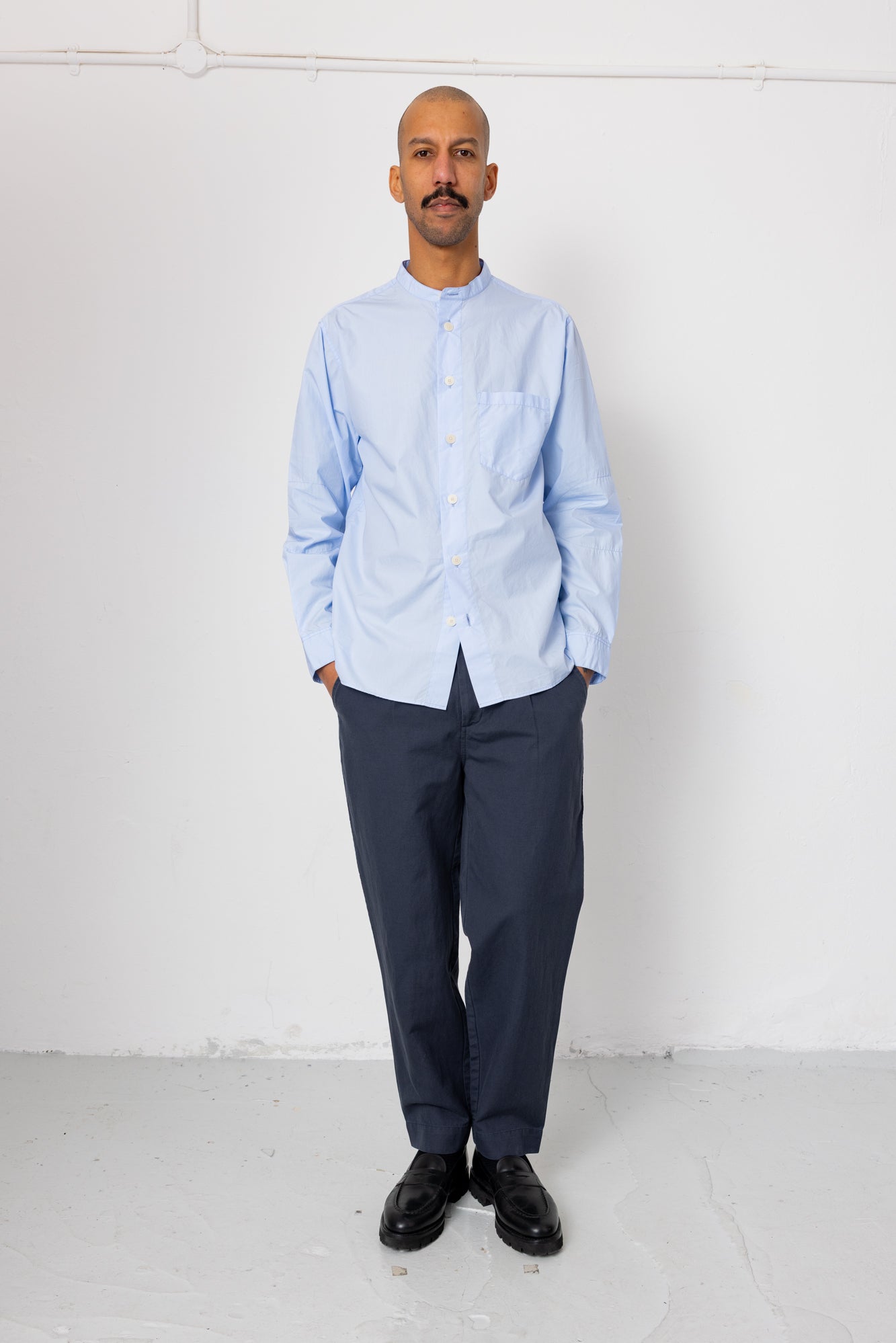 Man wearing a light blue shirt and dark pants against a white background
