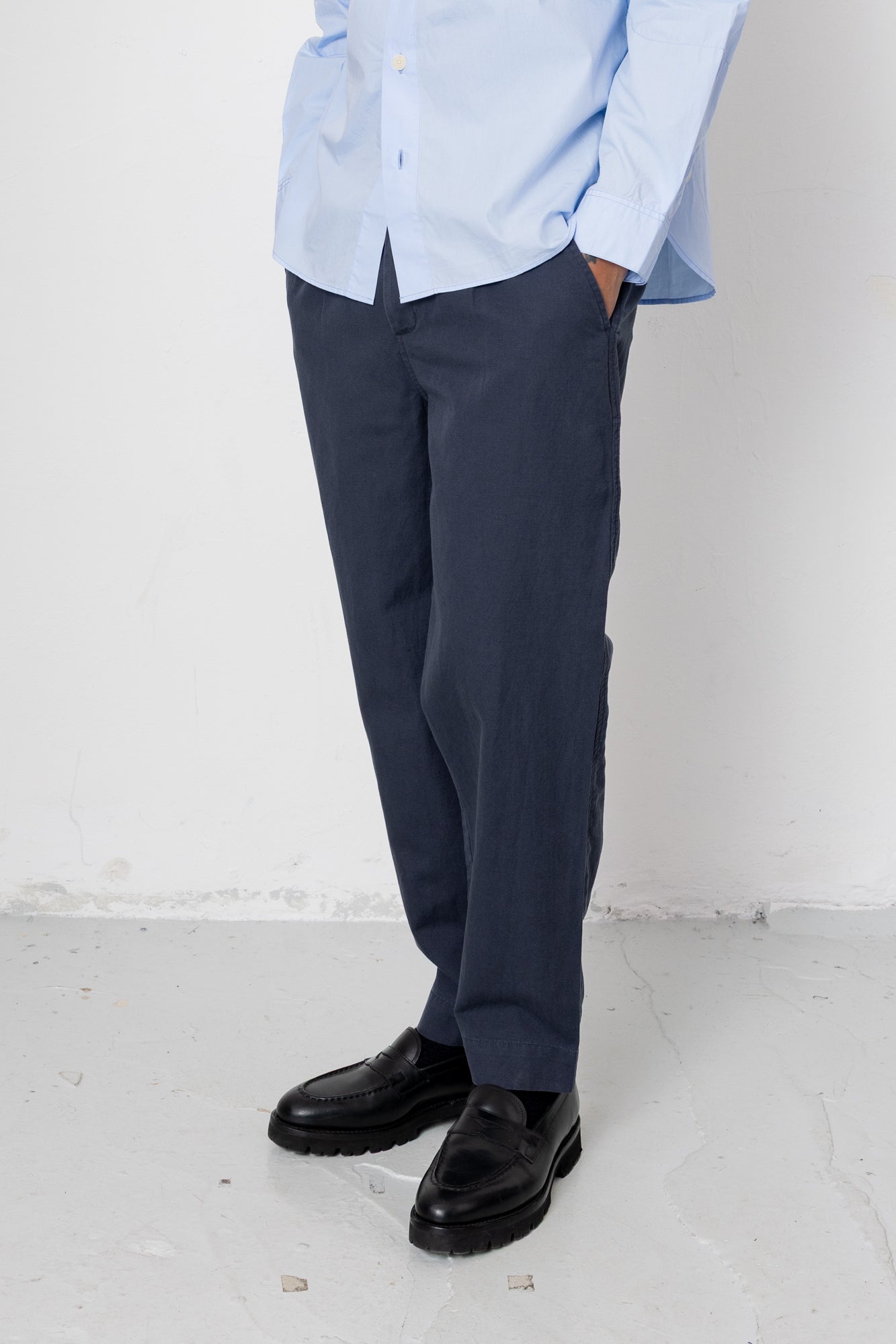 Person wearing a light blue shirt, dark pants, and black shoes on a white background