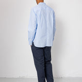 Man wearing a light blue shirt and dark pants against a white wall