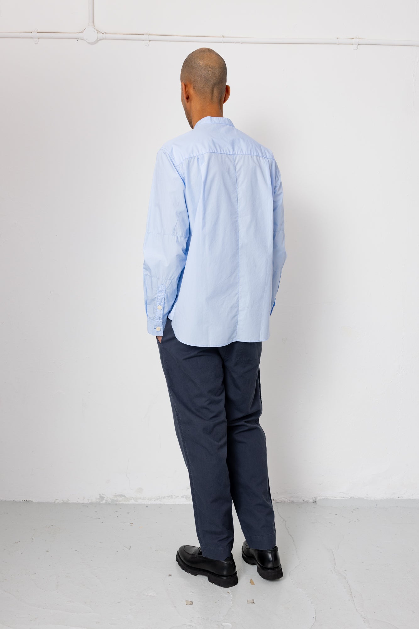 Man wearing a light blue shirt and dark pants against a white wall