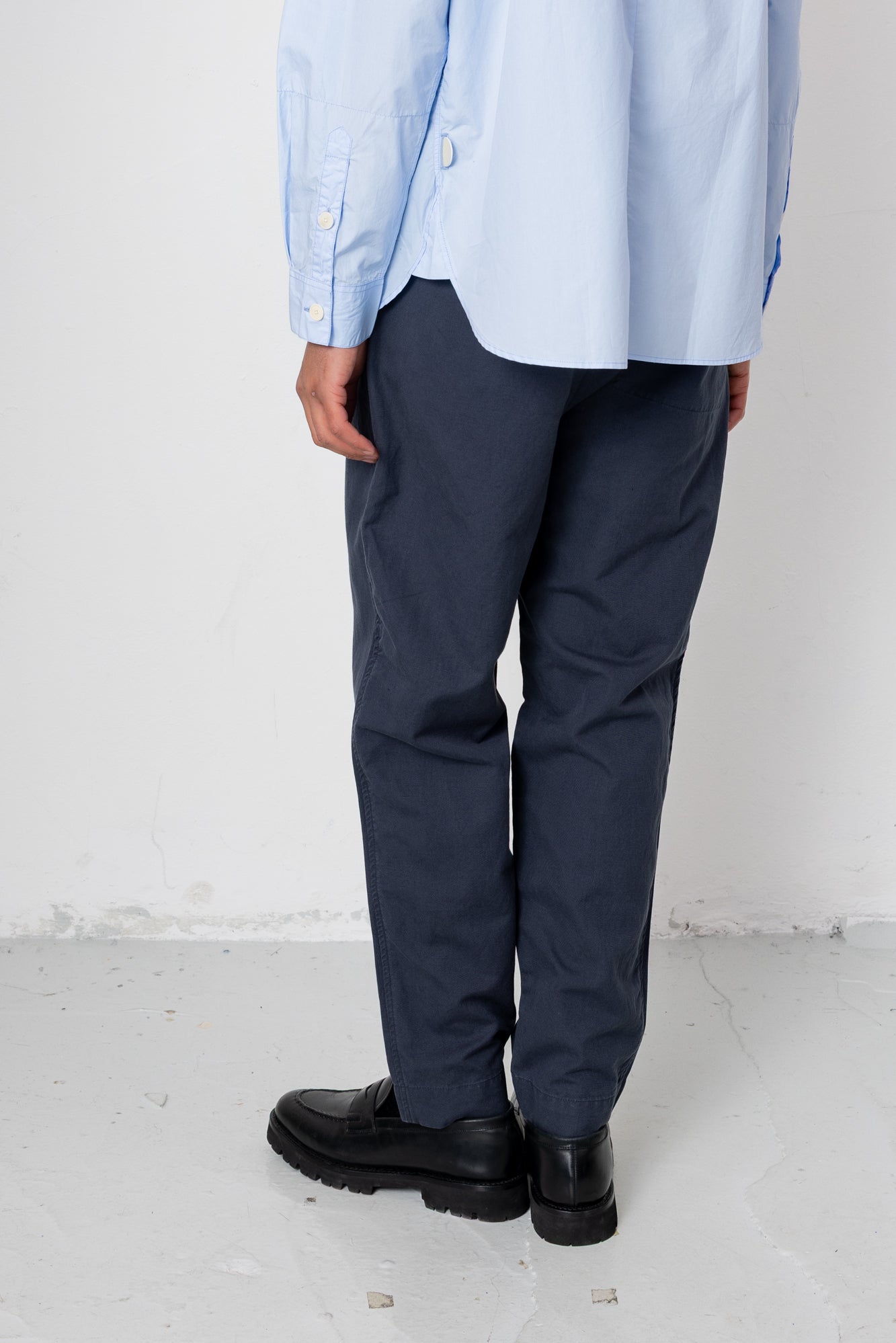 Person wearing a light blue shirt, navy pants, and black shoes on a white background