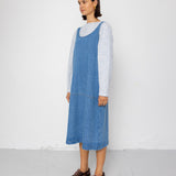 Woman wearing a blue denim dress over a striped shirt on a white background