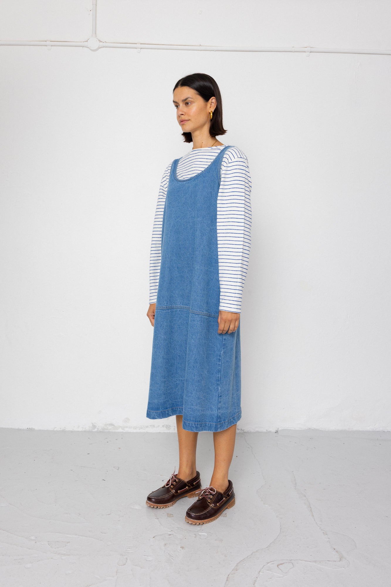 Woman wearing a blue denim dress over a striped shirt on a white background
