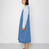 Person wearing a blue denim dress over a striped shirt against a white background