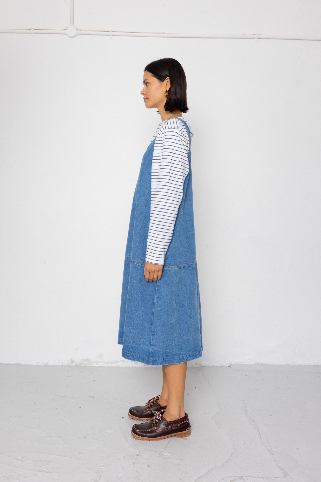Person wearing a blue denim dress over a striped shirt against a white background