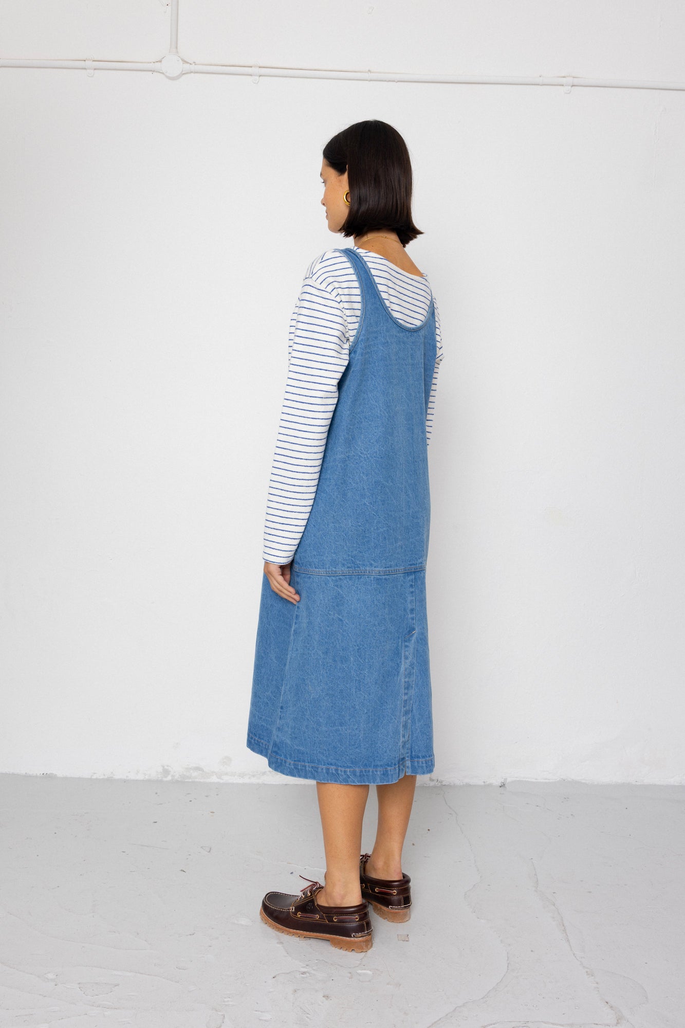 Person wearing a blue denim dress over a striped shirt against a white background