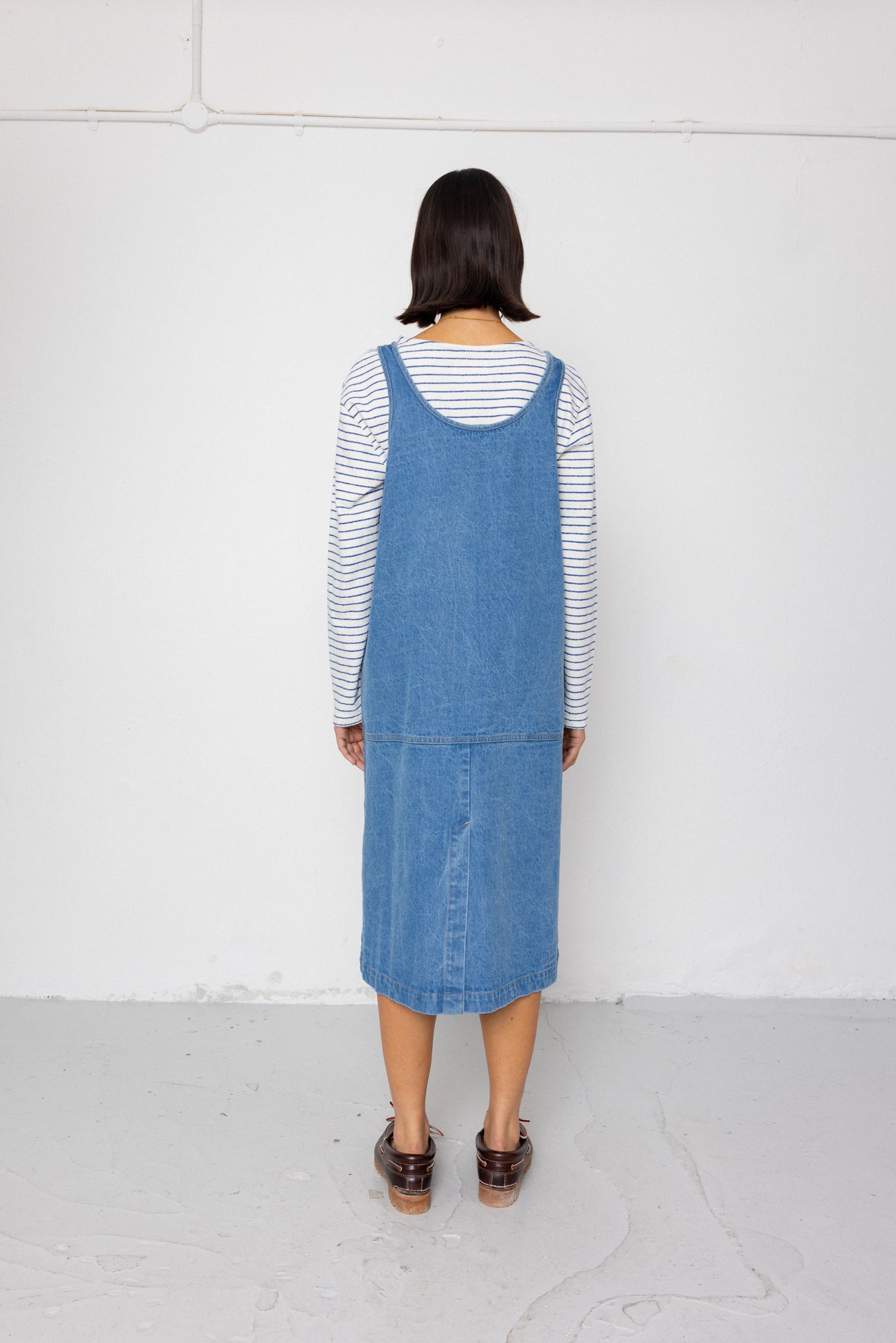 Woman wearing a blue denim dress over a striped shirt against a plain background