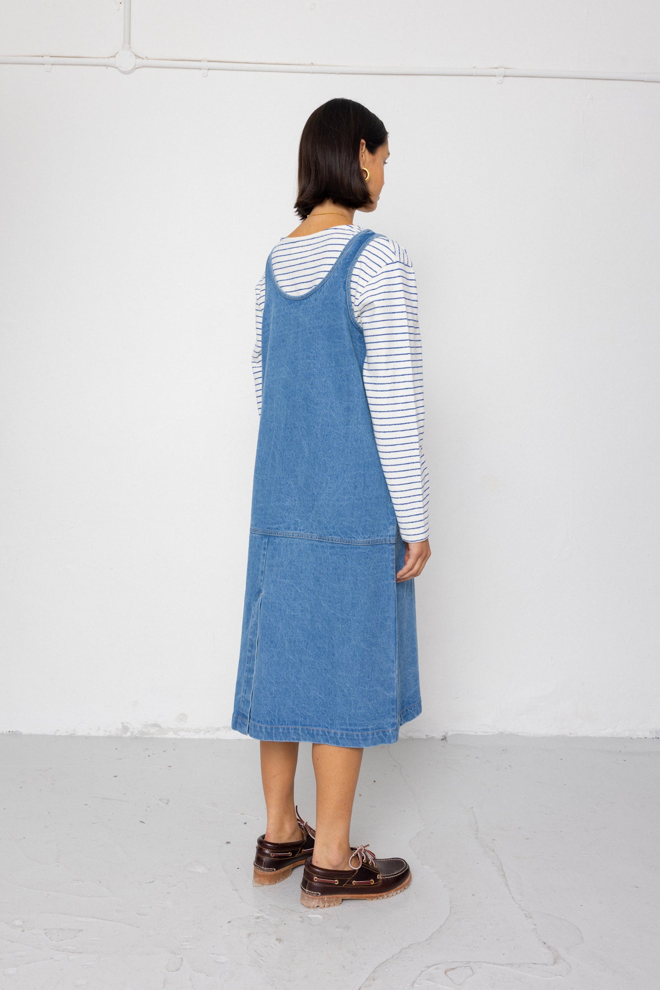Woman wearing a blue denim dress over a striped shirt against a plain background