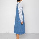 Woman wearing a blue denim dress over a striped shirt against a plain background