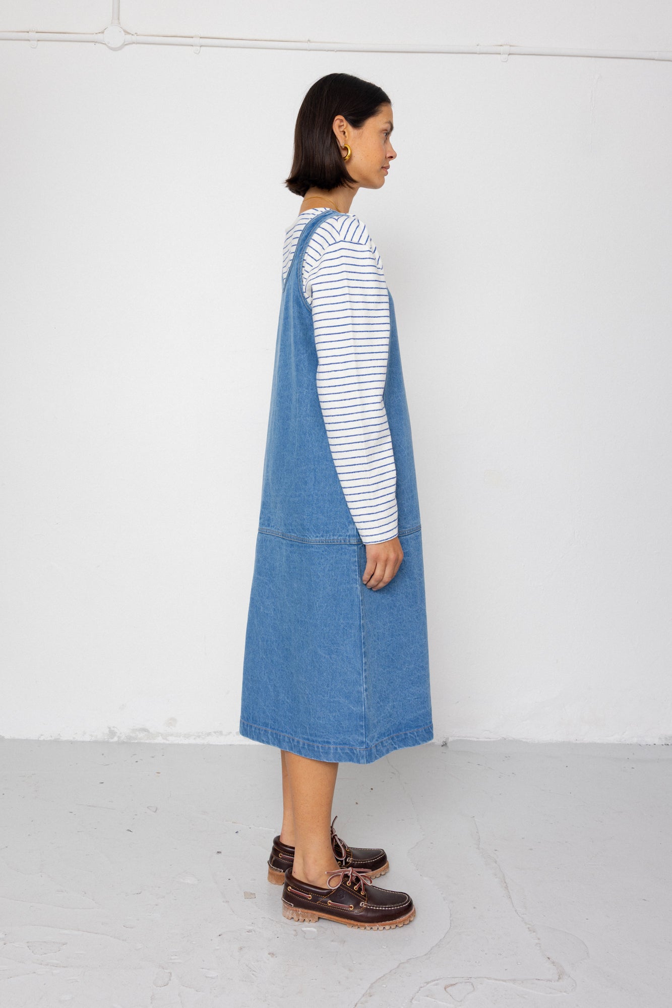 Woman wearing a blue denim dress over a striped shirt against a plain background