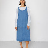 Person wearing a blue denim dress over a striped shirt on a white background