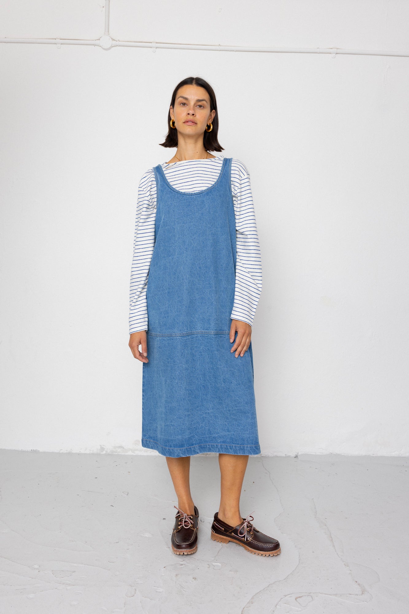 Person wearing a blue denim dress over a striped shirt on a white background