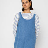 Woman wearing a blue denim dress over a striped shirt against a plain background