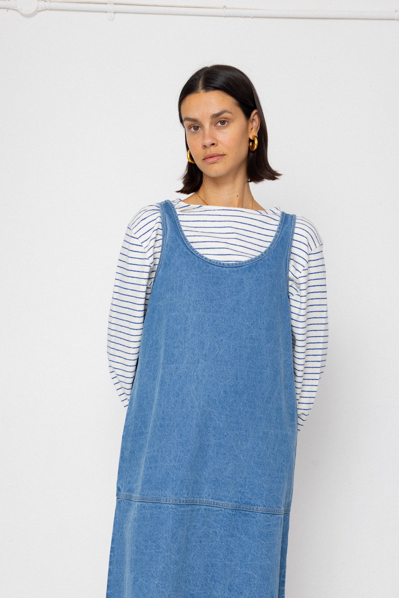 Woman wearing a blue denim dress over a striped shirt against a plain background