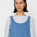 Woman wearing a blue denim dress over a striped shirt against a plain background