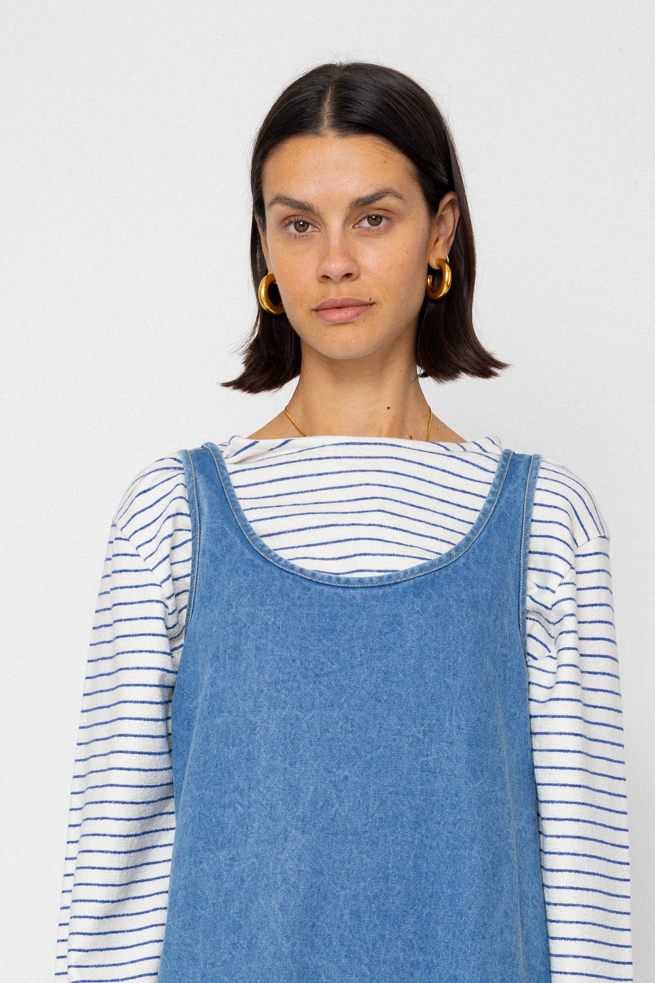 Woman wearing a blue denim dress over a striped shirt against a plain background