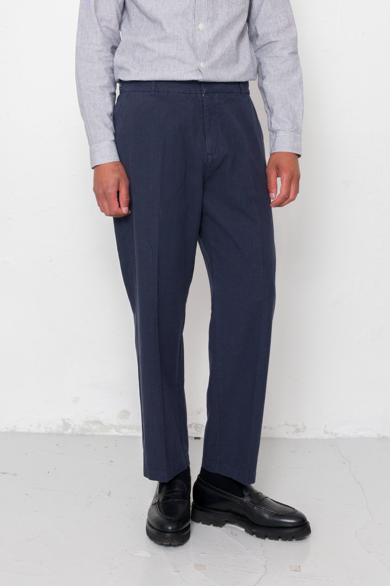 Person wearing navy pants and a light gray shirt against a white background
