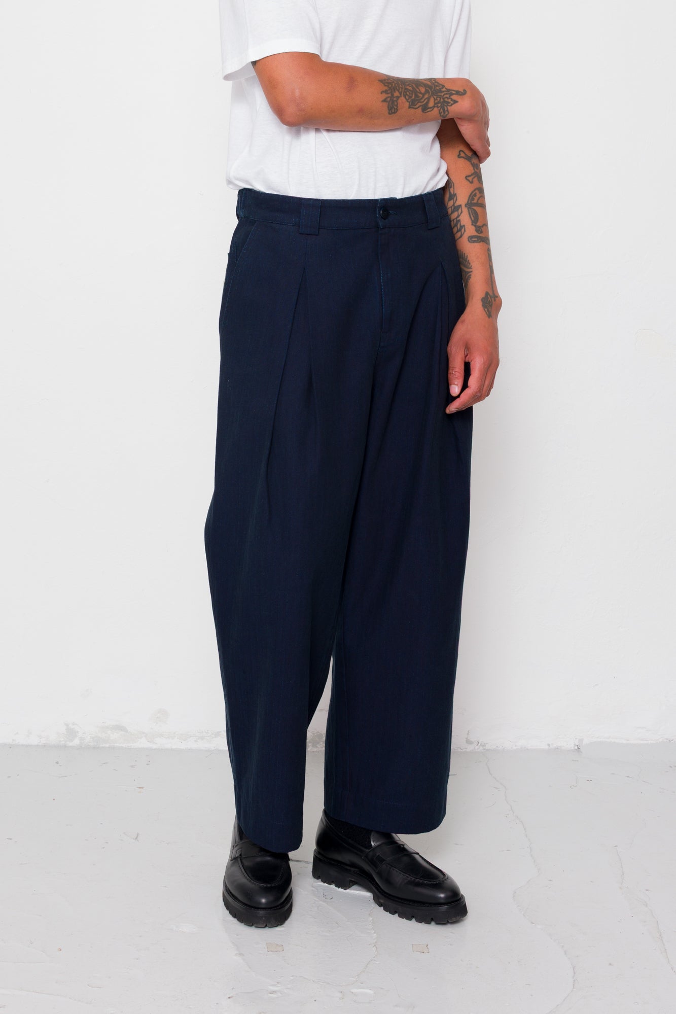 Person wearing navy pleated pants and black shoes on a white background