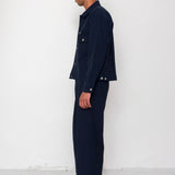 Man wearing a navy outfit with a blue cap against a white wall