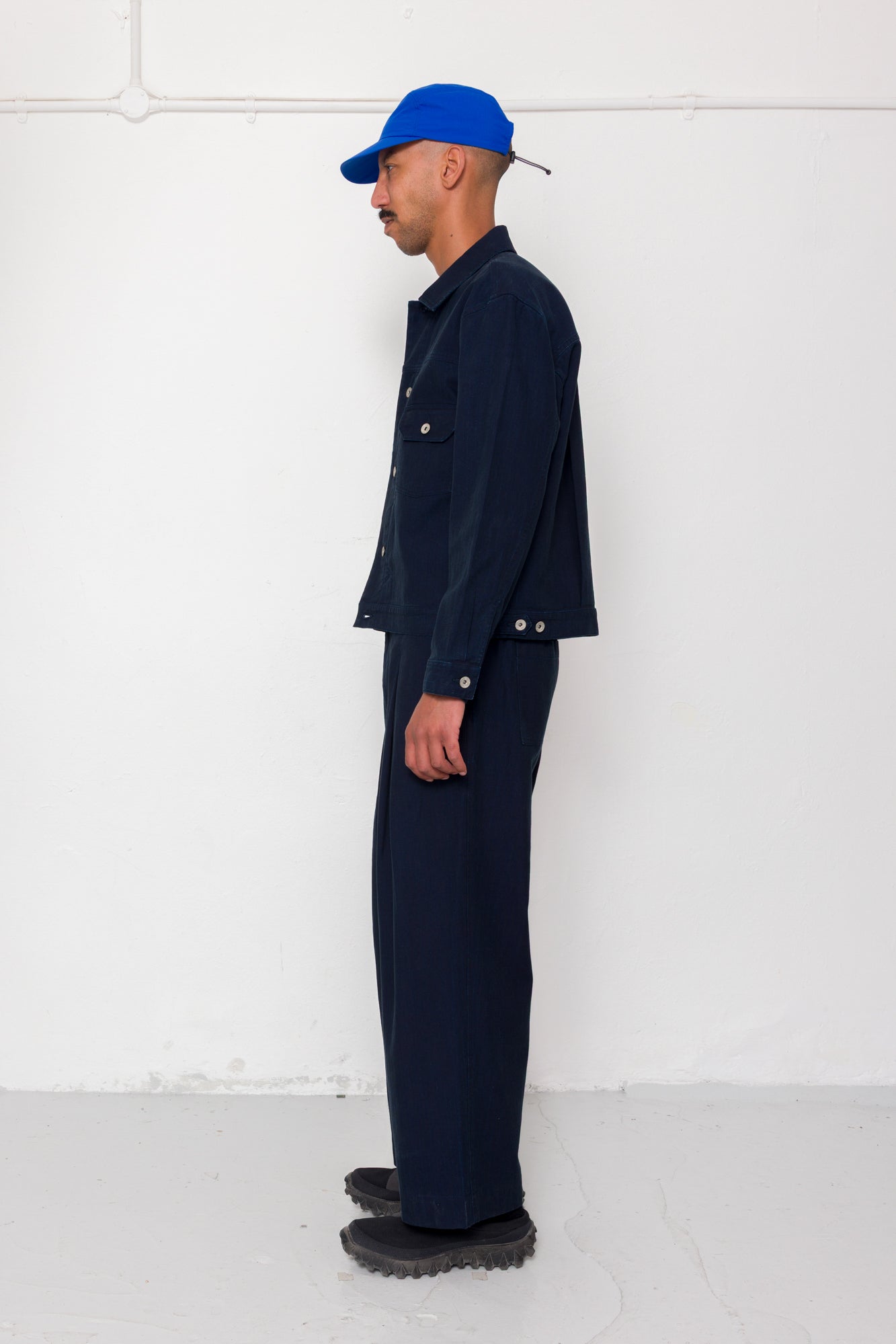 Man wearing a navy outfit with a blue cap against a white wall