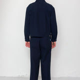 Person wearing a navy jacket & trousers with a blue cap against a white background
