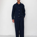 Man wearing a navy blue outfit with a cap against a white wall