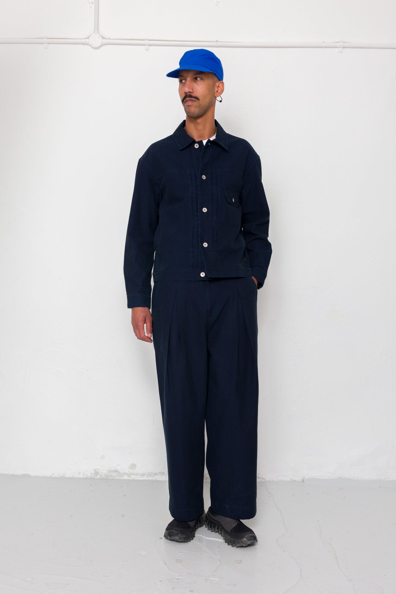 Man wearing a navy blue outfit with a cap against a white wall