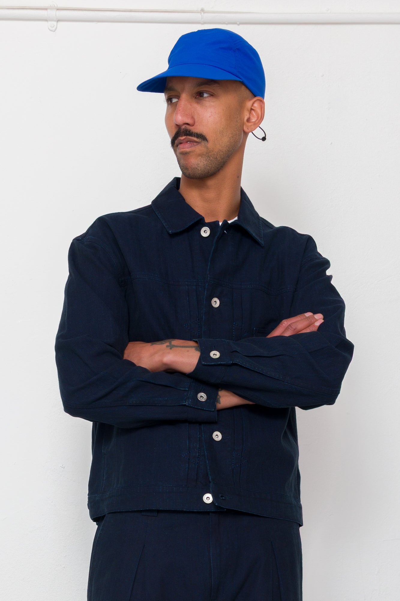 Man wearing a navy jacket and blue cap against a white background