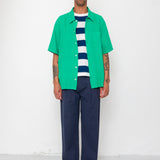 Man wearing a green shirt over a striped sweater with navy pants against a white background
