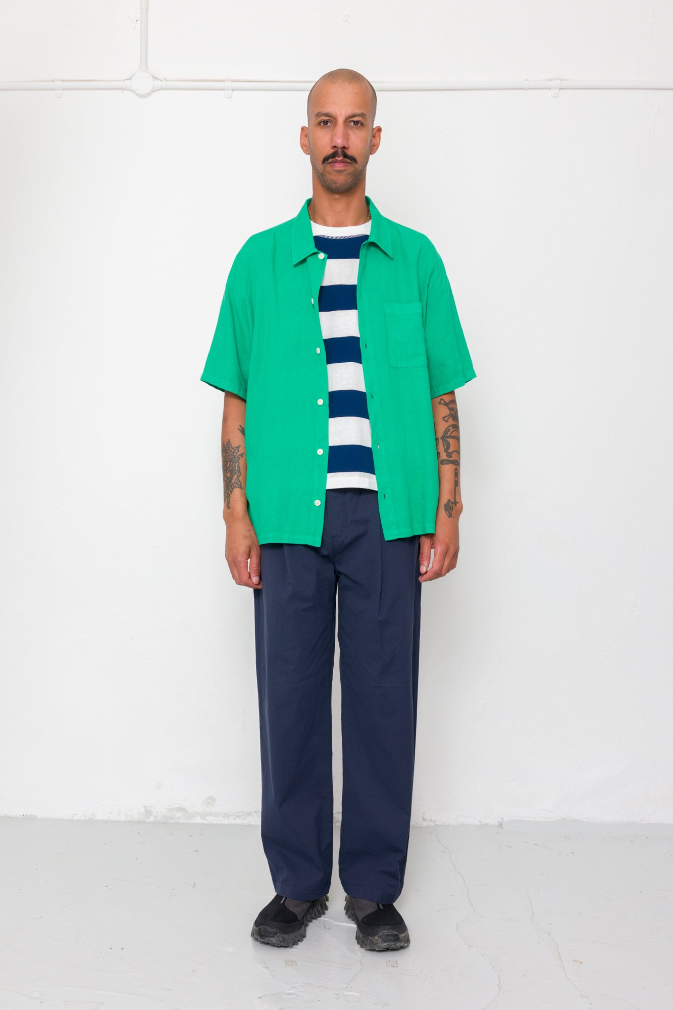 Man wearing a green shirt over a striped sweater with navy pants against a white background