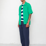Man wearing a green shirt, striped sweater, and navy pants against a white background