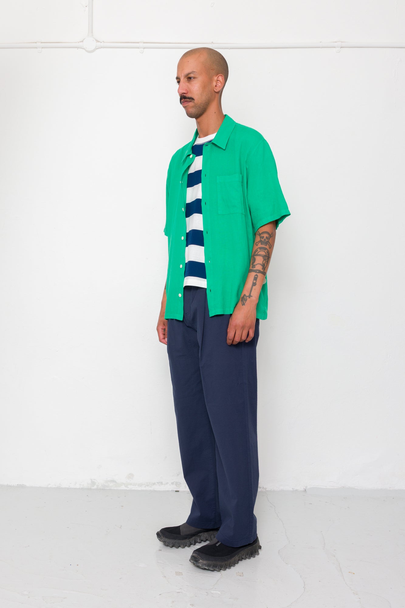 Man wearing a green shirt, striped sweater, and navy pants against a white background