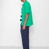 Person wearing a green shirt and blue pants standing against a white wall.