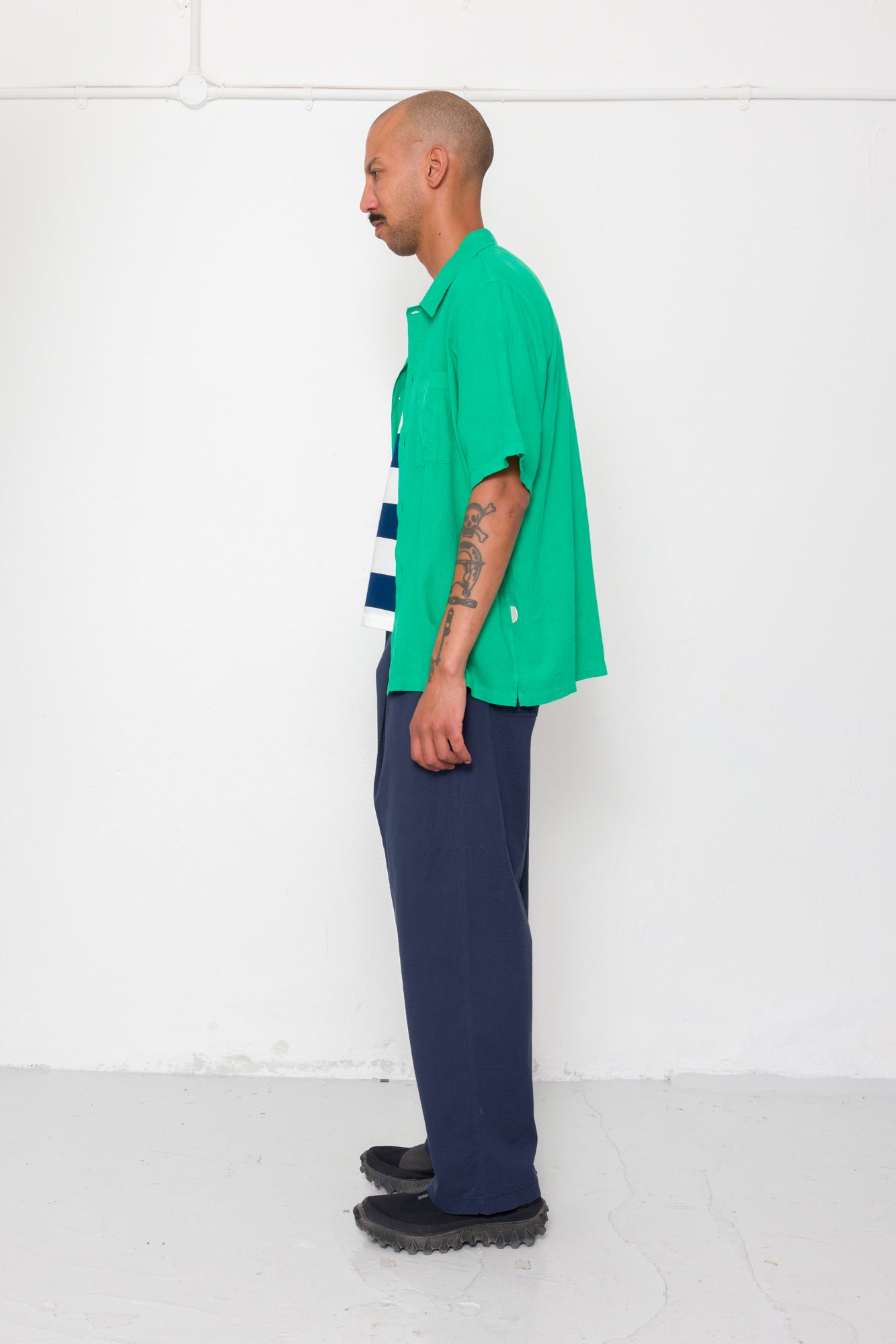 Person wearing a green shirt and blue pants standing against a white wall.