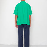 Person wearing a green shirt and navy pants standing against a white wall.