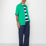 Man wearing a green shirt over a striped sweater with navy pants against a white background