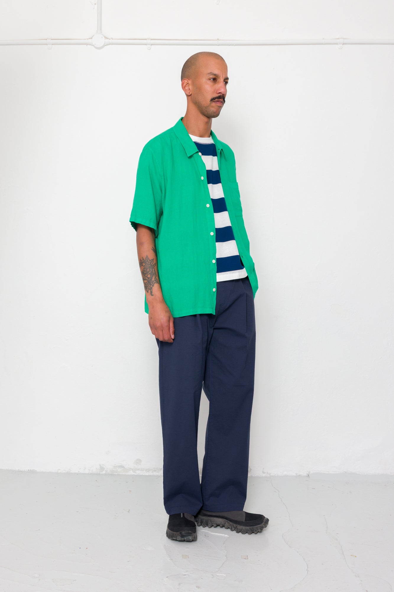 Man wearing a green shirt over a striped sweater with navy pants against a white background