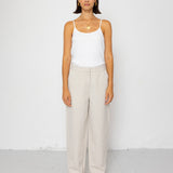 Woman wearing a white tank top and beige pants against a white background