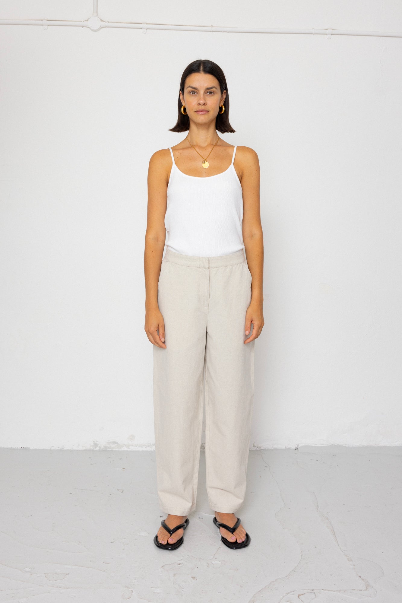 Woman wearing a white tank top and beige pants against a white background