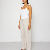 Woman wearing a white tank top and beige pants against a white background