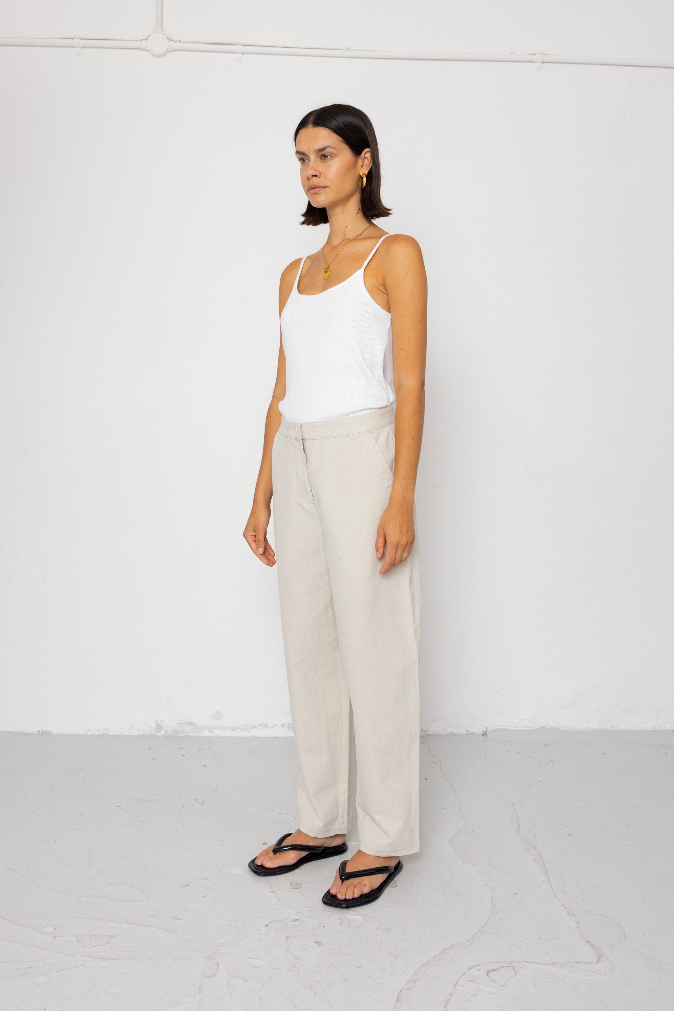 Woman wearing a white tank top and beige pants against a white background
